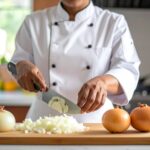 廚師在明亮廚房中示範洋蔥切法，桌上擺著切絲、切丁、切圈三種洋蔥造型，刀具與砧板整潔乾淨