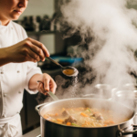 料理鍋中冒著熱氣，廚師正用量匙加入鹽調整味道